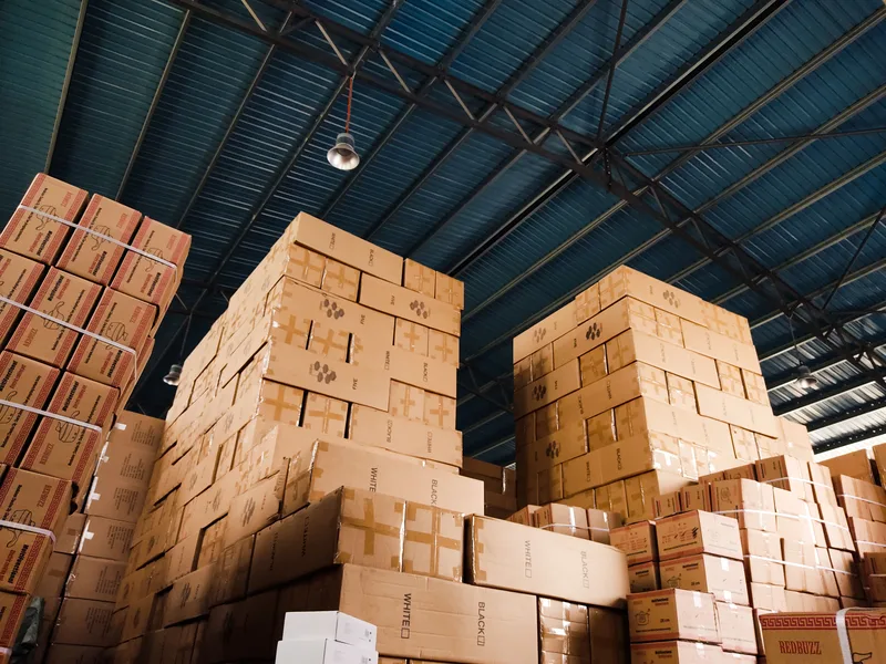 High stacks of cardboard boxes organized in a warehouse with a blue metal ceiling