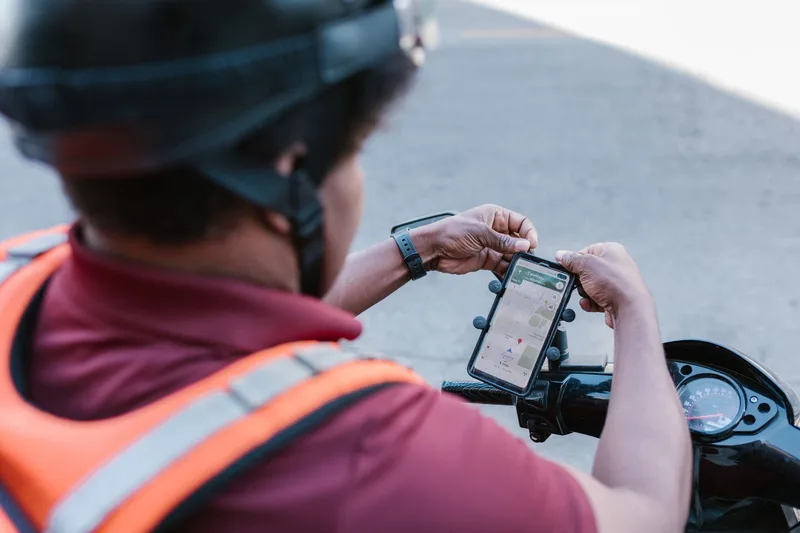 Delivery courier on a scooter checking a smartphone during an outdoor delivery run