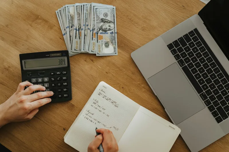 Seller using a calculator and notebook to work out shipping cost per package