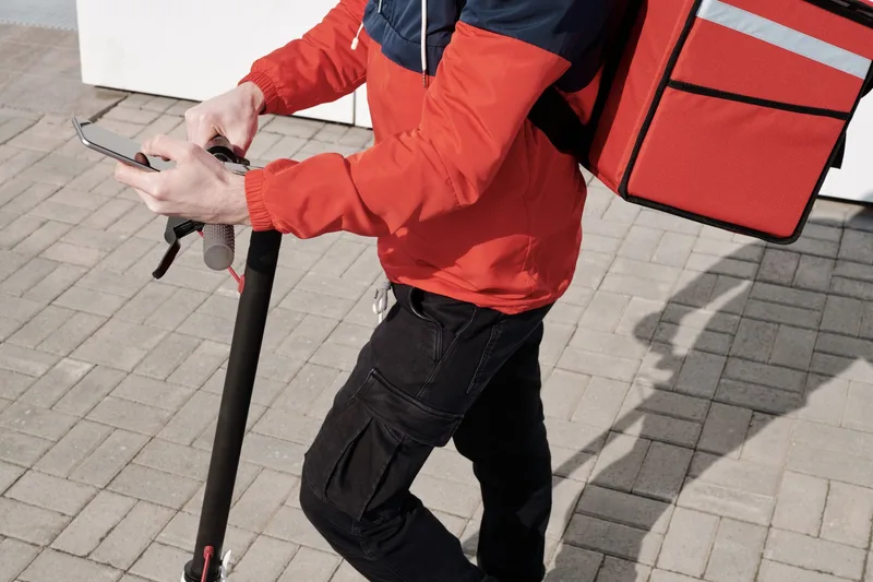 Delivery courier on a scooter checking a smartphone during an outdoor delivery run
