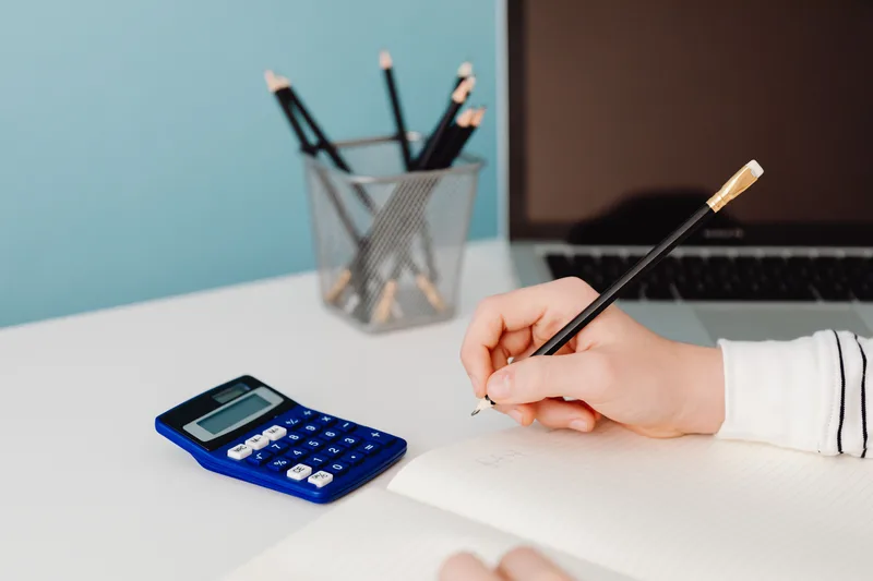 Seller using a calculator and notebook to work out shipping cost per package