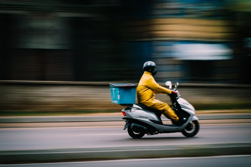 A delivery rider transporting parcels by motorcycle through a city street