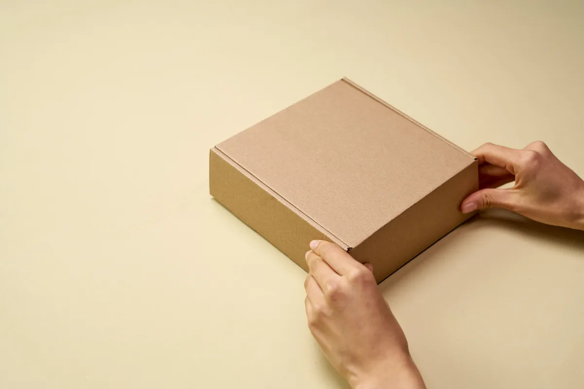 Hands sealing a plain cardboard shipping box before courier pickup