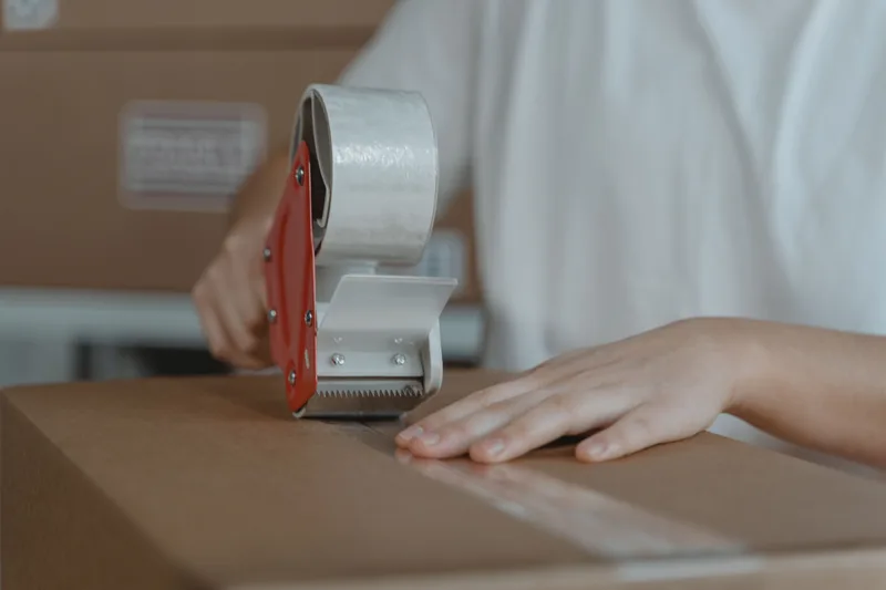 Hands using a tape dispenser to seal a cardboard box for shipping